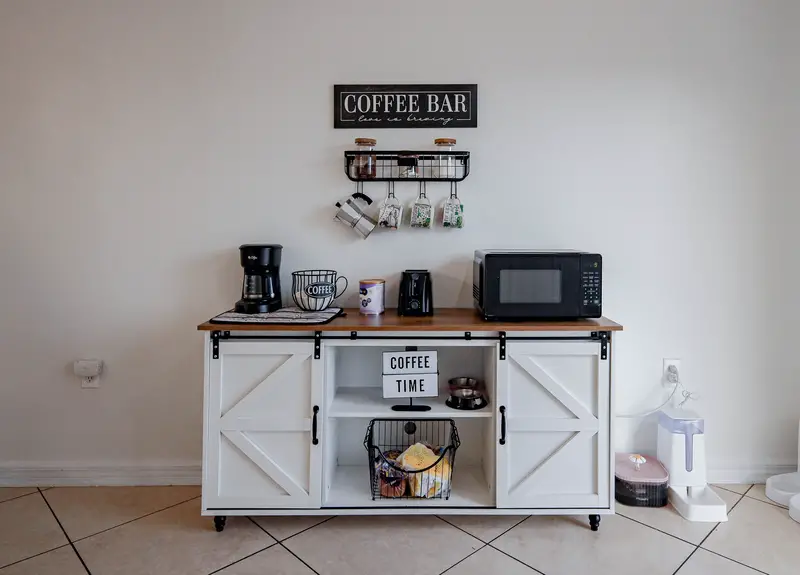 Modern coffee bar setup featuring a coffee maker, microwave, and decorative items on a white cabinet