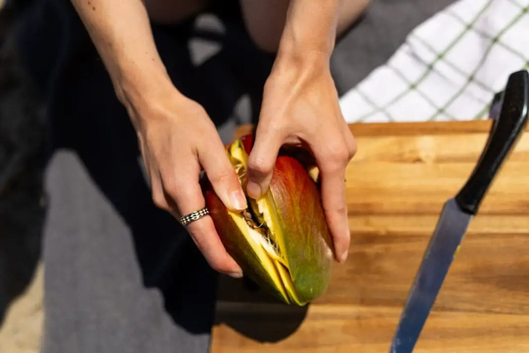 Hands peeling a ripe mango on a wooden cutting board
